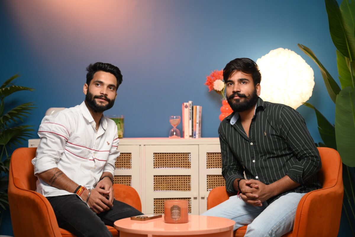 Two men seated in orange chairs on a blue podcast set at Sooper Studios in Noida