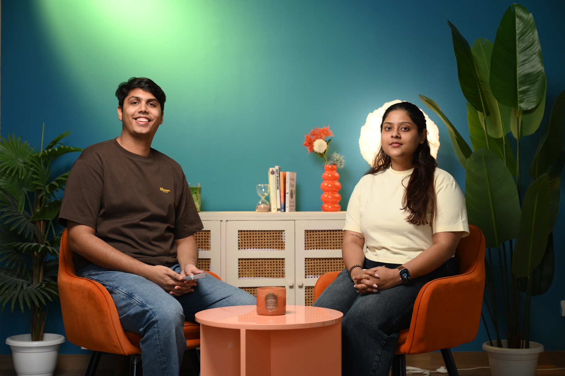 Man and woman seated in orange chairs on a teal podcast set at Sooper Studios in Noida