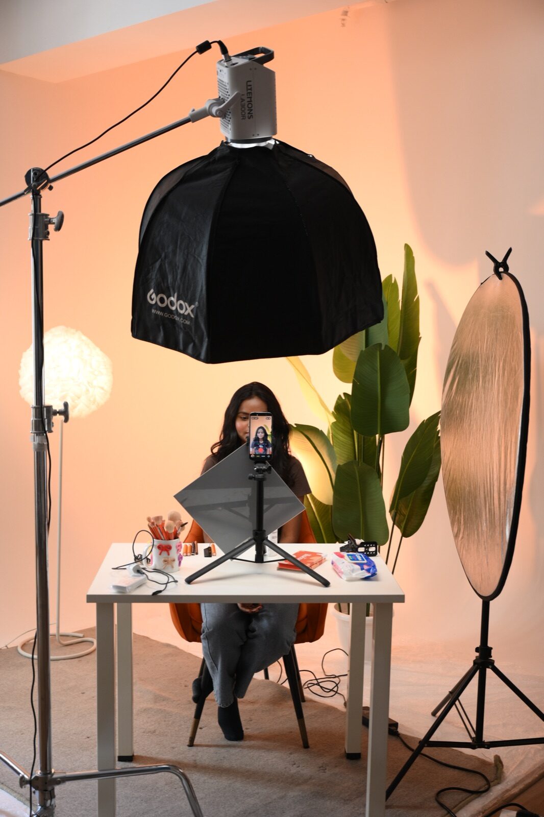 Behind-the-scenes studio setup with a camera, softbox, reflector and seated presenter