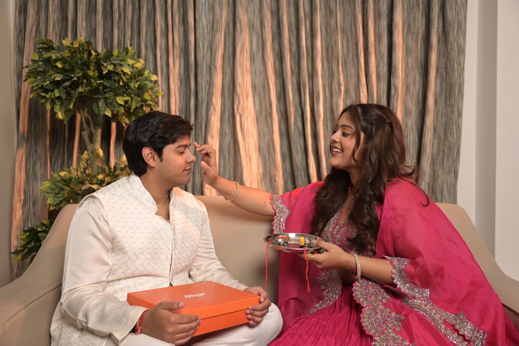 Brother and sister celebrating Rakhi with a gift box on a styled set