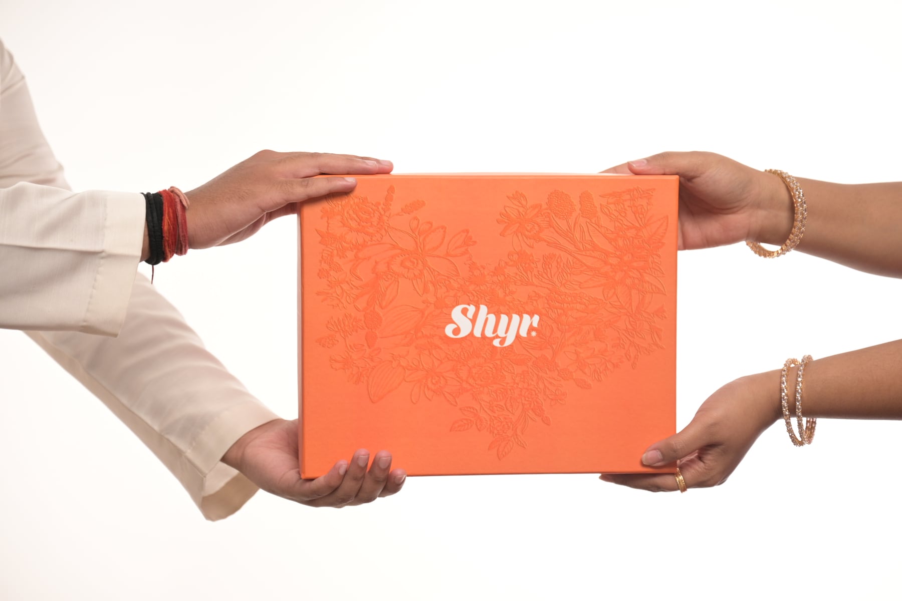 Hands exchanging an orange Rakhi gift box against a clean white background