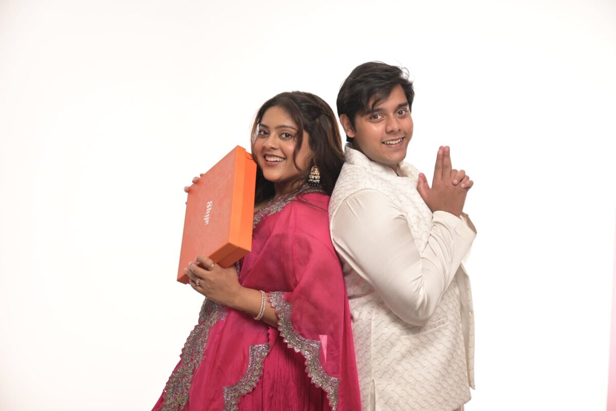 Brother and sister posing with an orange Rakhi gift box on a clean studio set at Sooper Studios in Noida