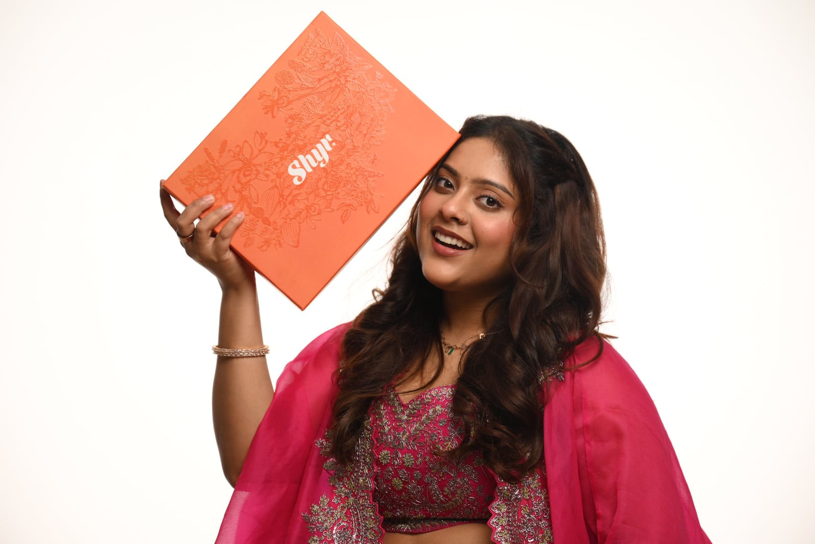Woman smiling while presenting an orange Rakhi gift box