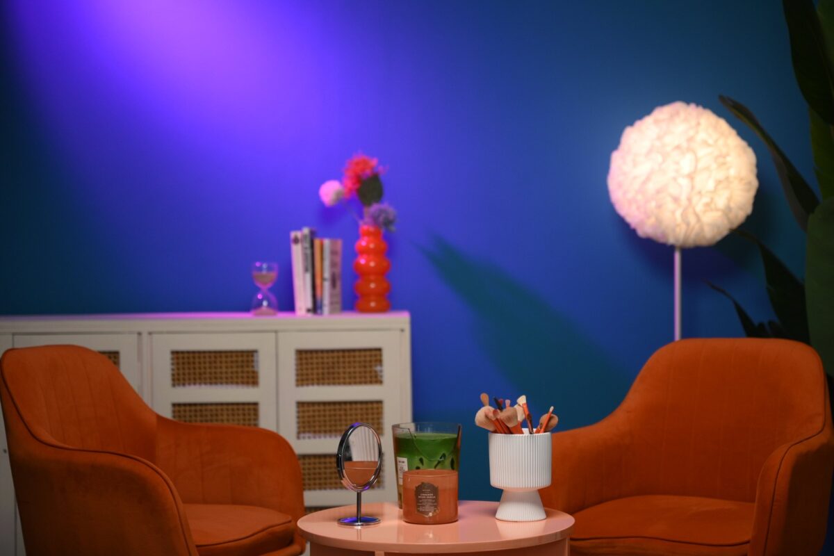 Styled teal studio wall with orange chairs pink table mirror makeup brushes cabinet and practical lamp at Sooper Studios in Noida